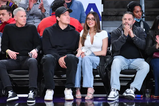 Madison Beer sitting with a group courtside wearing jeans and platform heels.