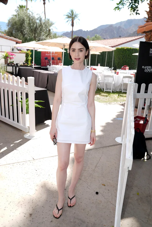 Lily Collins standing outside in a white dress and flip-flops.