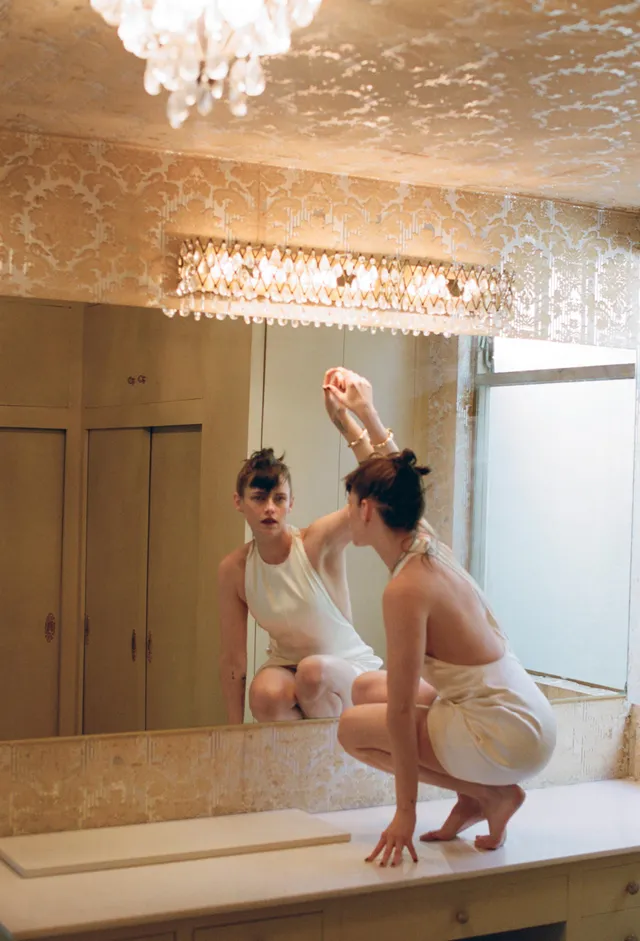 Kristen Stewart crouching barefoot beside a mirror.