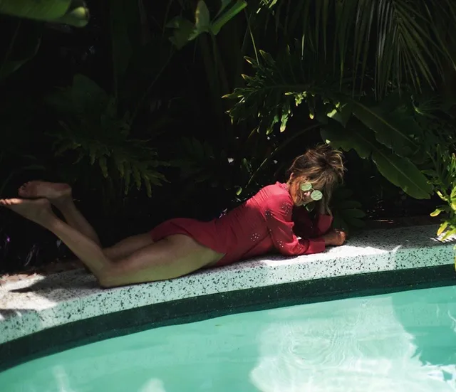 Halle Berry reclining barefoot beside a pool in a red outfit.