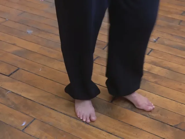 Naomi Scott a close detail of bare feet beneath dark trousers.