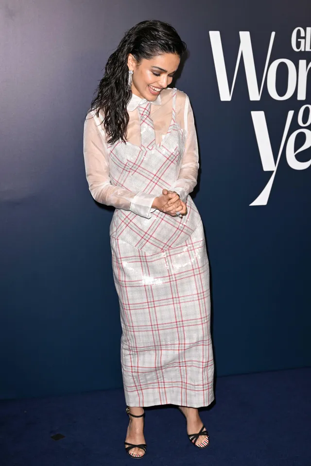 Rachel Zegler posing in a checked dress and black heels at an event.
