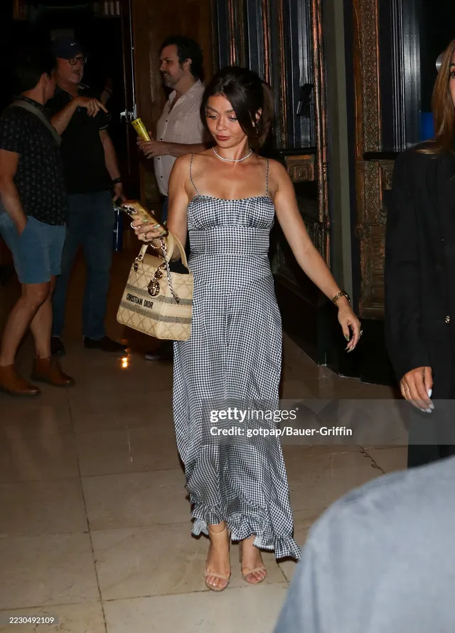 Sarah Hyland walking indoors in a grey dress and heels.