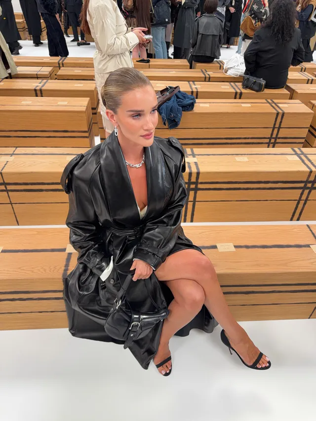 Rosie Huntington-Whiteley a seated black coat and heels on steps.