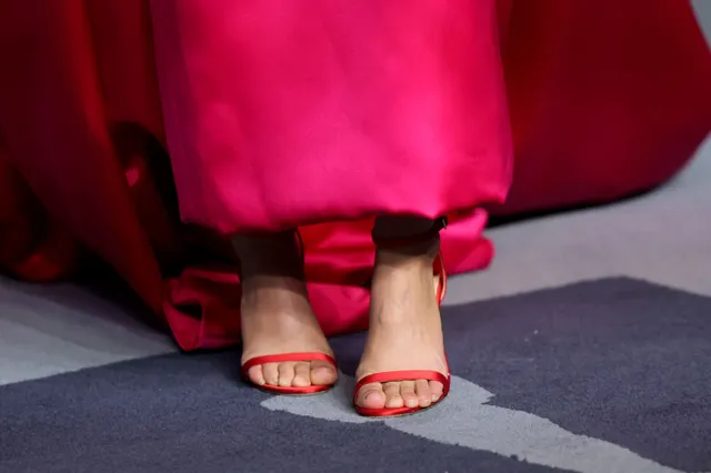 Rachel Zegler wearing red open-toe heels beneath a red gown.