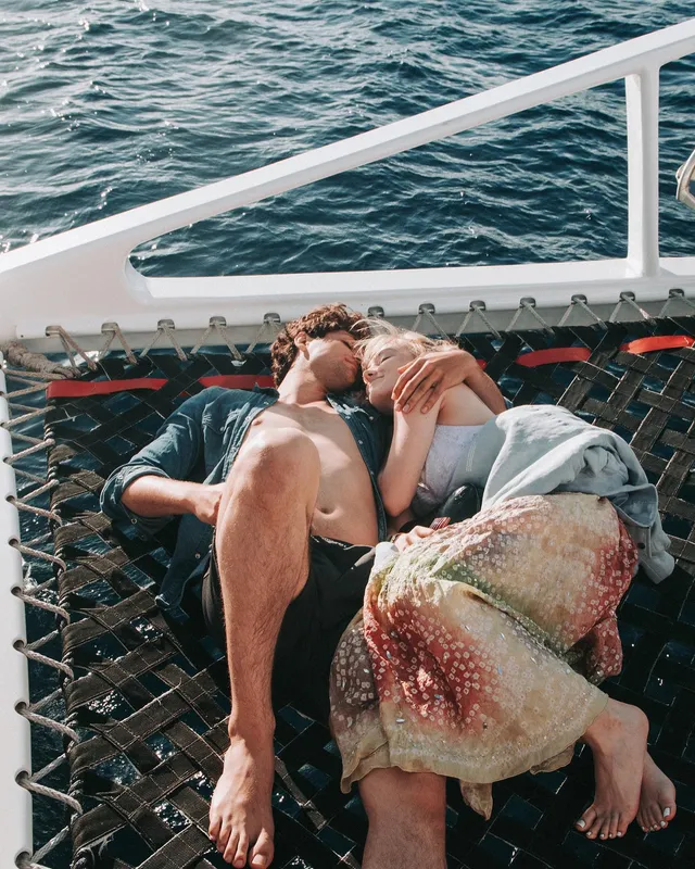 Meg Donnelly reclining barefoot with a companion on a catamaran net.