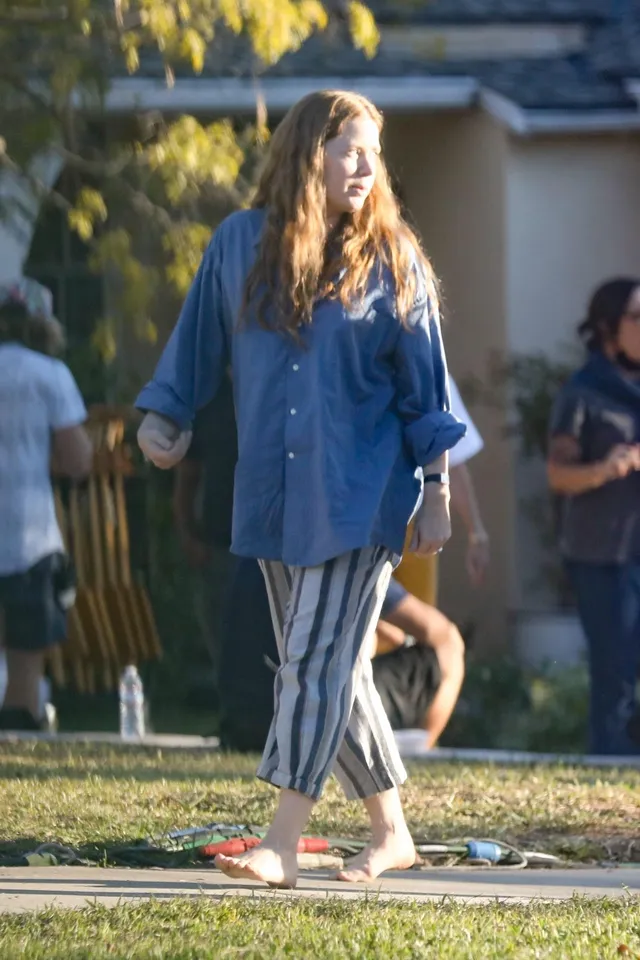 Amy Adams standing outside in a blue shirt and striped trousers.