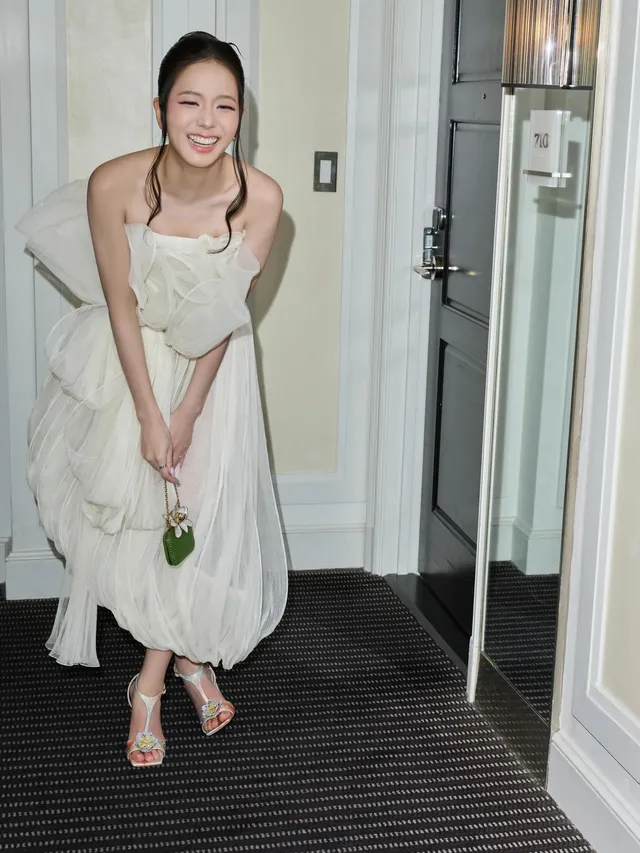Jisoo smiling in pale heeled sandals and a light dress in a doorway.