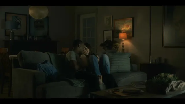 Victoria Pedretti sitting on a sofa with a companion during a screen scene.