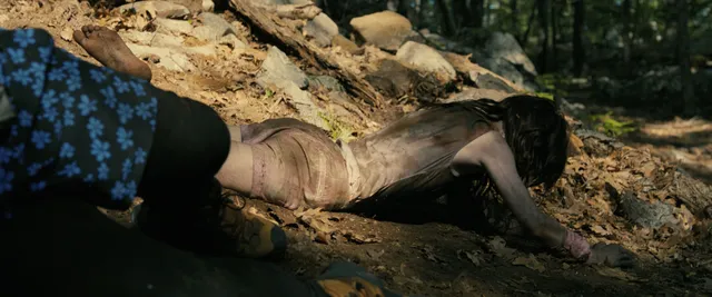 Sophie Thatcher reaching forward on a woodland floor in a film scene.