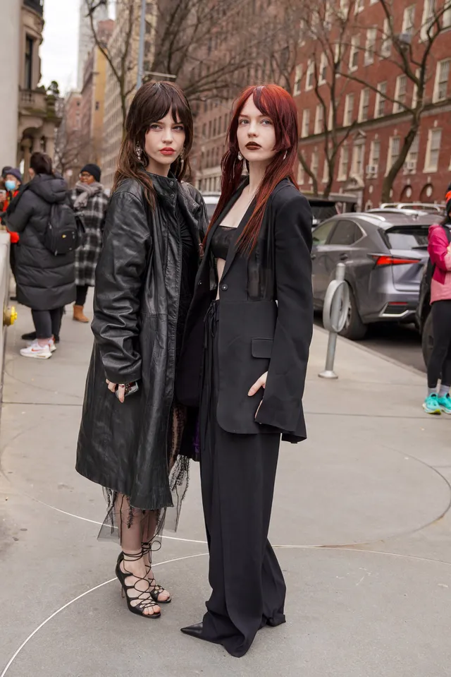 Sophie Thatcher standing beside another woman in a black outfit and strappy heels.