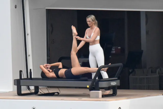 Kylie Jenner stretching barefoot on an exercise machine beside an instructor.