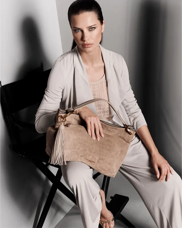 Adriana Lima sitting in a pale suit and metallic heels for a portrait.