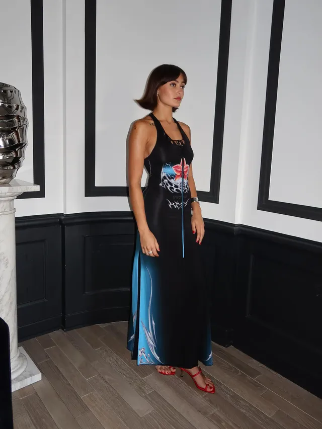 Ella Purnell standing indoors in a dark outfit and red sandals.