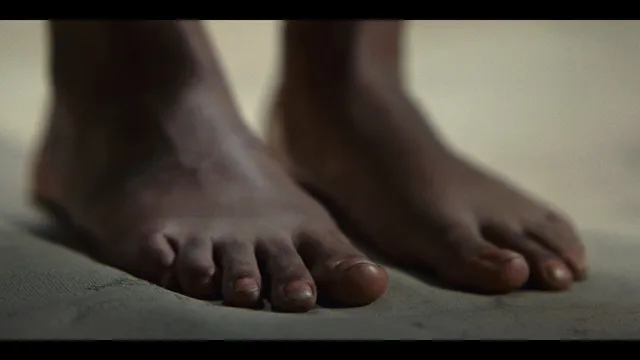 Sophie Wilde standing barefoot on a padded surface in a film scene.