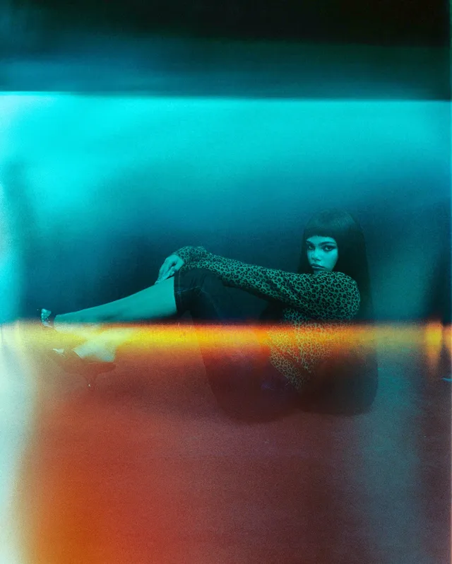 Ariana Greenblatt reclining in a patterned outfit on a colored studio surface.