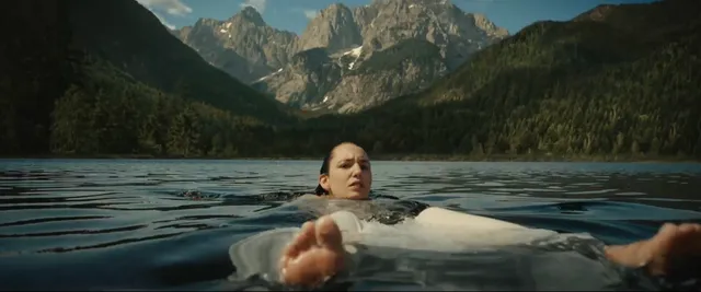 Sophie Nélisse floating in a lake with bare feet facing the camera.
