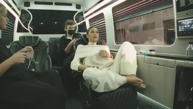 Shay Mitchell sitting on a train in a white outfit with white socks.