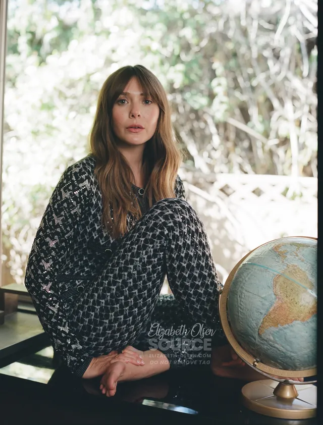 Elizabeth Olsen sitting barefoot beside a globe in a patterned outfit.