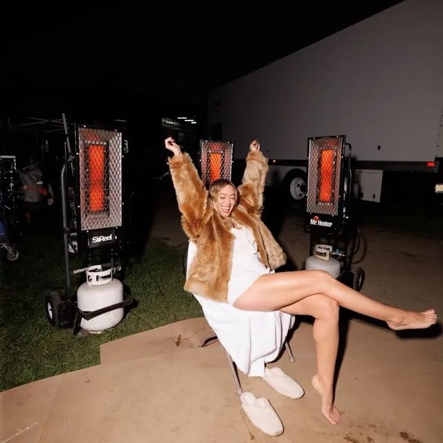 Hilary Duff sitting barefoot outdoors in a pale dress and jacket.