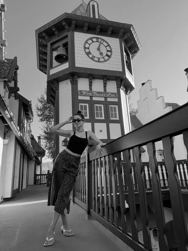 Vanessa Hudgens standing beside a clock tower in heels for a monochrome photograph.