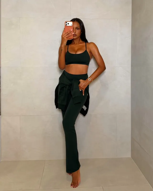 Jasmine Tookes taking a barefoot mirror photograph in a black top and dark trousers.