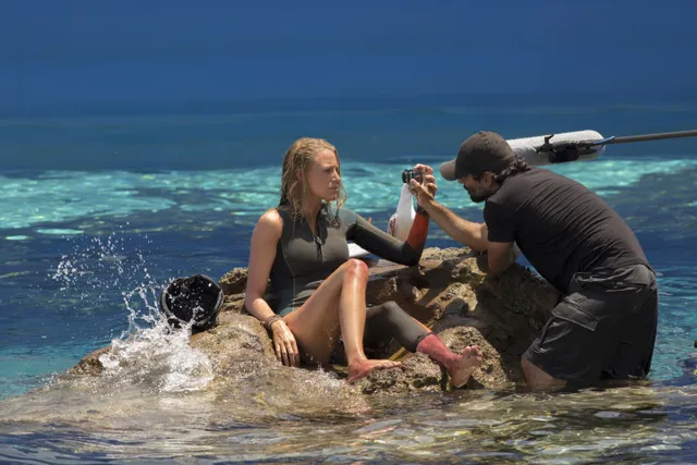 Blake Lively seated barefoot on seaside rocks during filming.