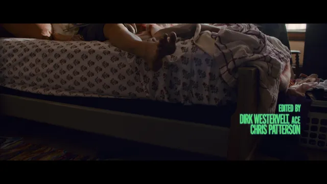 Samara Weaving reclining barefoot on a bed in a film scene.