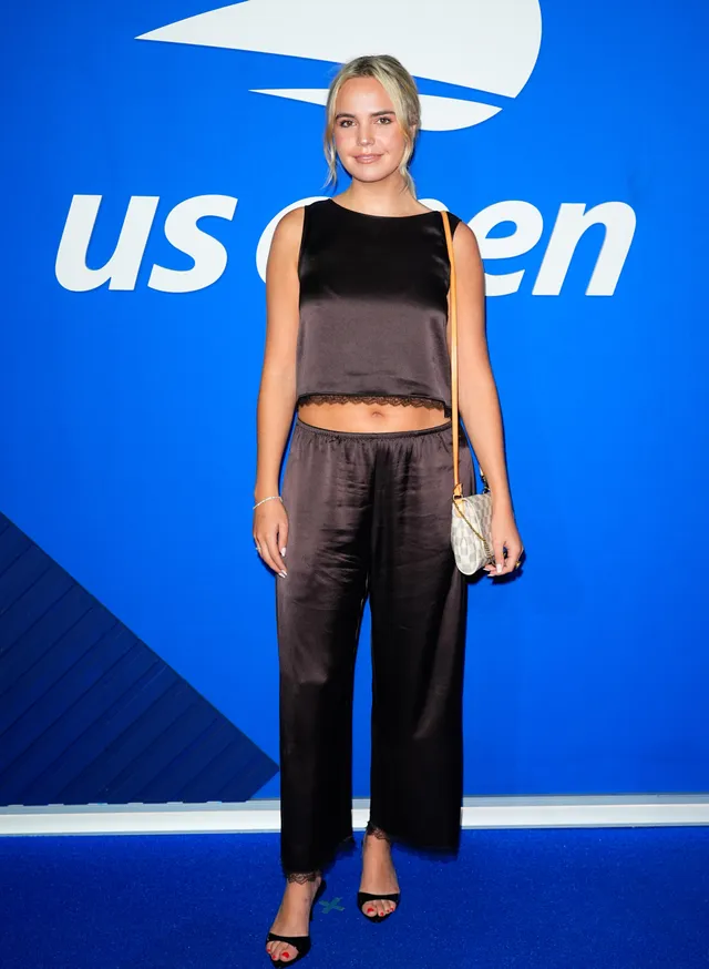 Bailee Madison posing in a dark satin outfit and black heels.