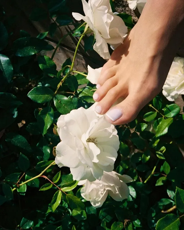 Rita Ora resting a bare foot beside white flowers.