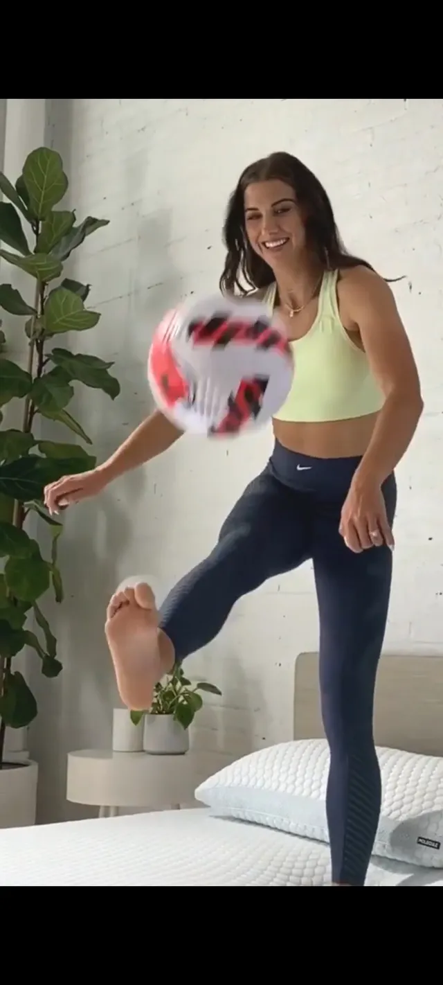 Alex Morgan balancing a football barefoot on a mattress.