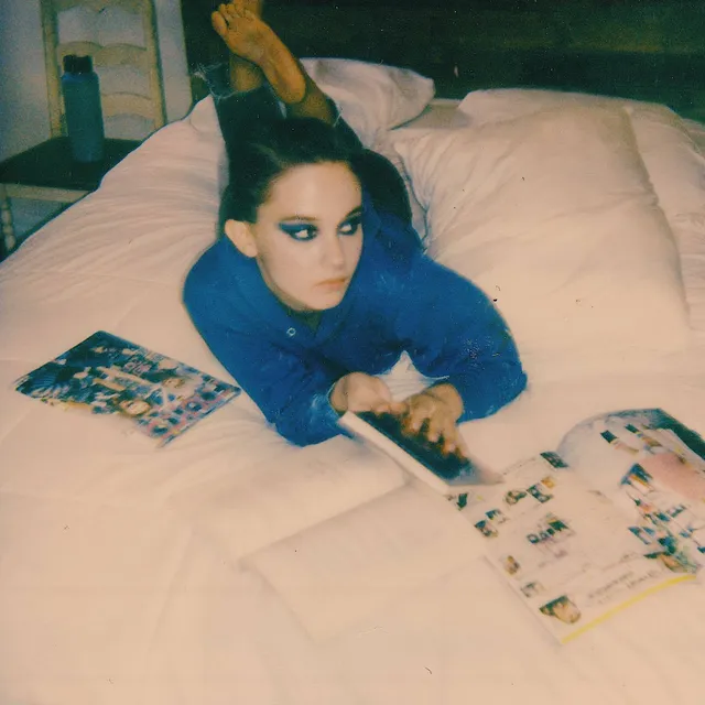 Cailee Spaeny lying on a bed with her bare feet raised.