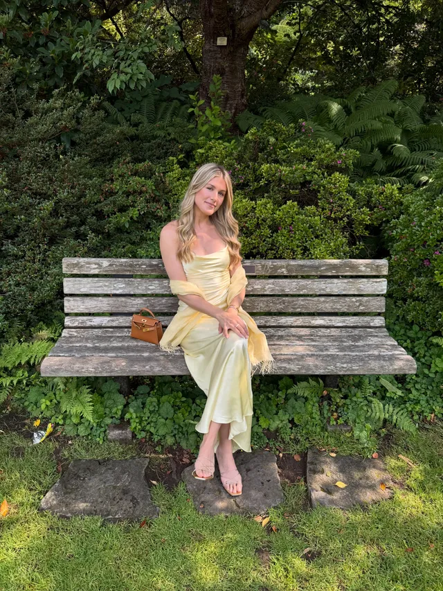 Eugenie Bouchard sitting in pale heels and a yellow dress on a wooden bench.