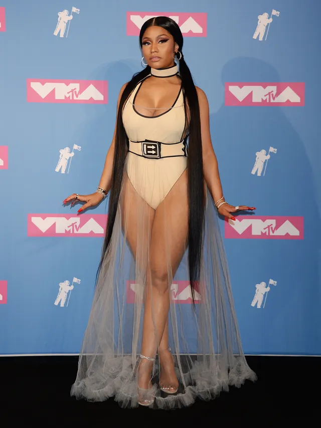 Nicki Minaj posing at an awards event in a pale outfit and sheer skirt.