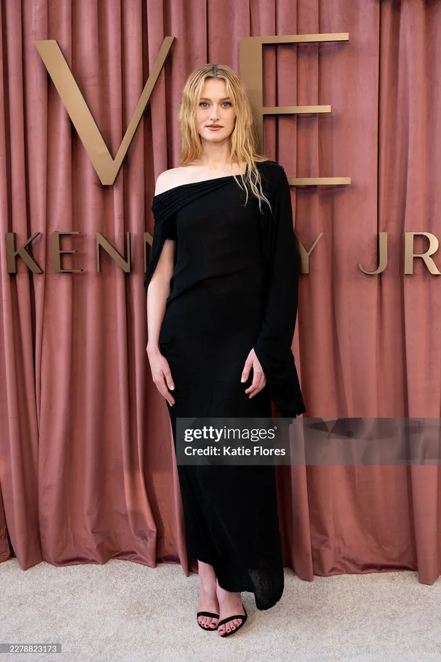 Sarah Pidgeon standing before a premiere backdrop in a black dress and heels.