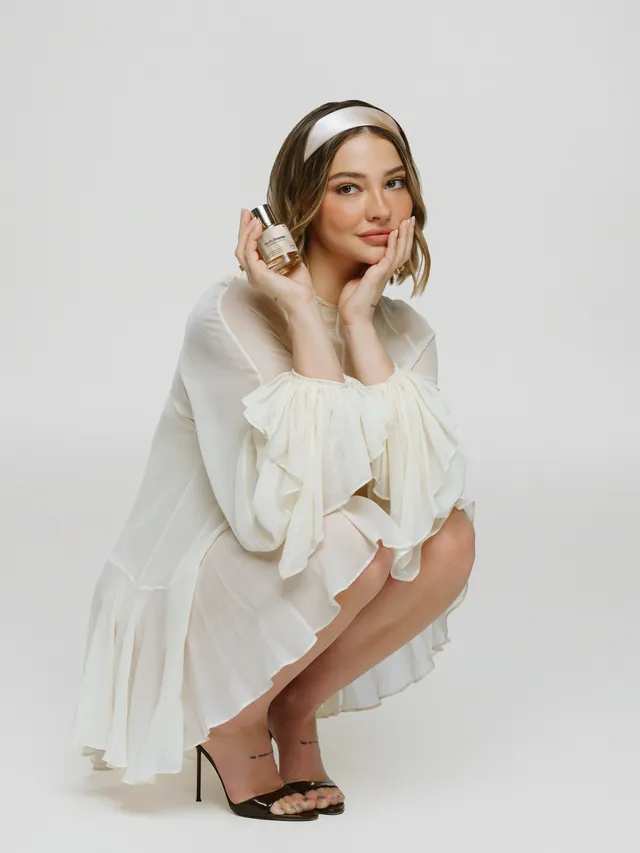 Madelyn Cline crouching in a white outfit with headphones and black heels.