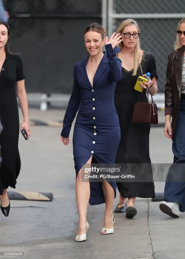 Rachel McAdams walking outdoors in a navy dress and white heels.
