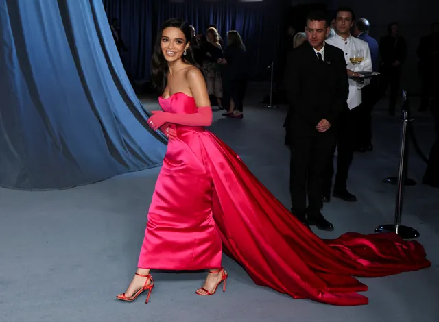 Rachel Zegler walking in a bright pink gown and red heels.
