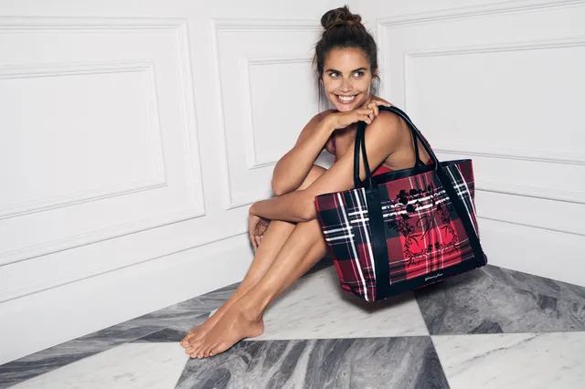 Sara Sampaio sitting barefoot beside a patterned handbag in a dark outfit.