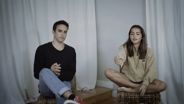 Isabela Merced sitting cross-legged beside a man during an interview.