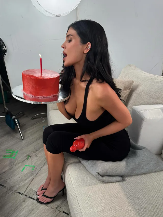 Kylie Jenner sitting on a sofa with a cake while wearing flip-flops.