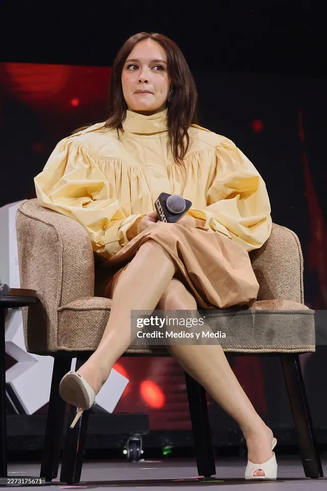 Olivia Cooke sitting onstage in white pumps.