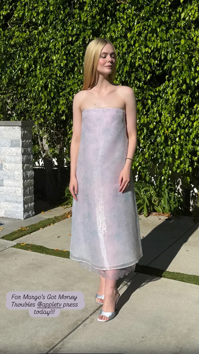 Elle Fanning posing outdoors in a pale pink dress and silver heels.