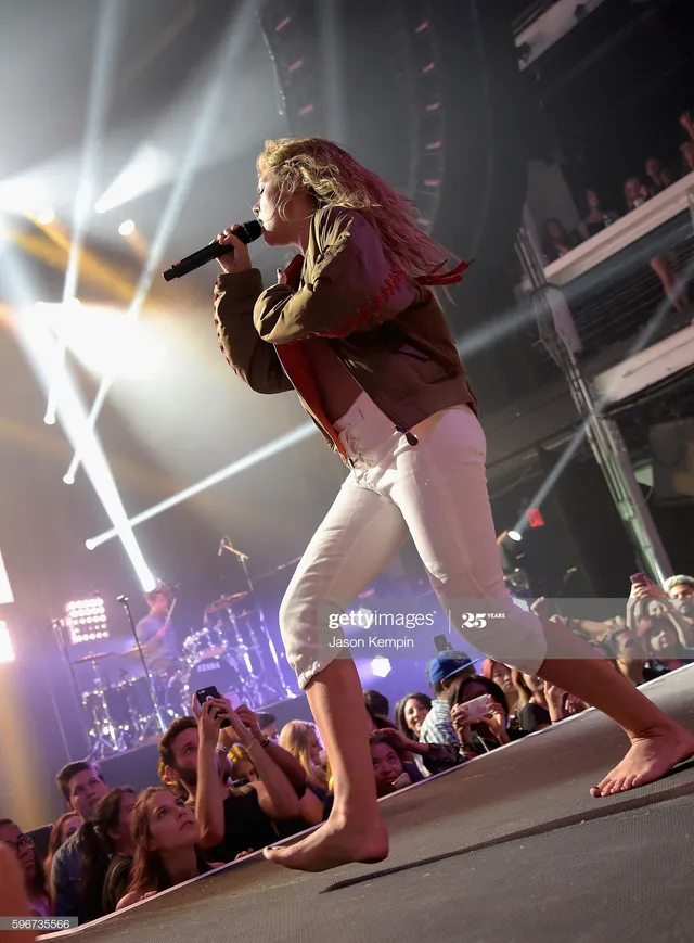 Tove Lo performing barefoot on stage in pale trousers.
