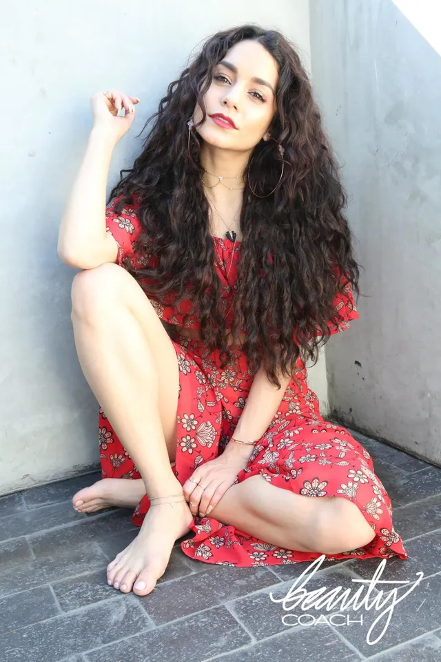 Vanessa Hudgens sitting barefoot in a red floral dress.