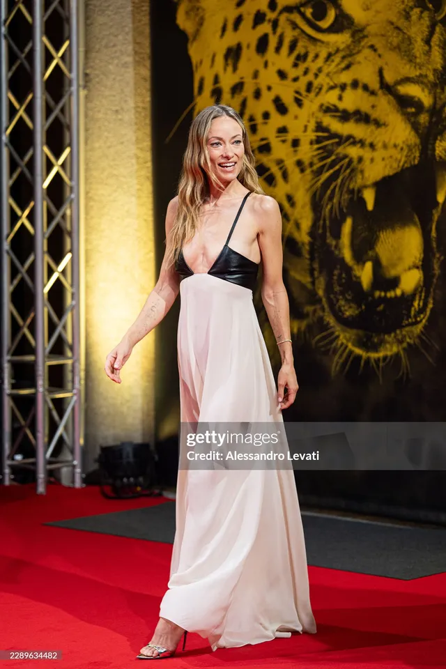 Olivia Wilde posing on a red carpet in a pale gown and metallic heels.