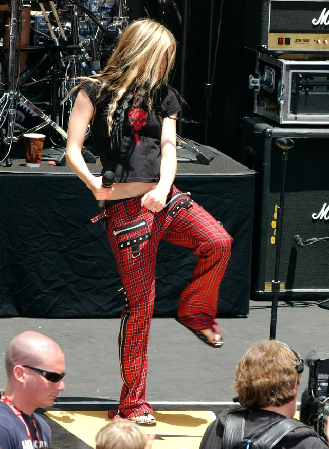 Avril Lavigne performing on stage in red trousers and flat sandals.