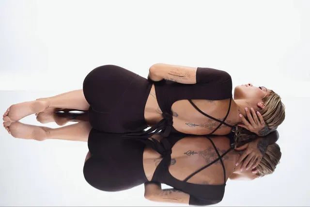 Rita Ora lying barefoot on a reflective studio floor.