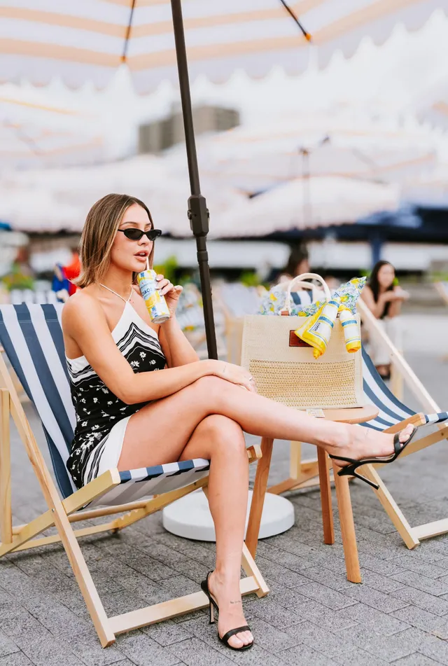 Madelyn Cline sitting outdoors in a striped deck chair wearing black heels.