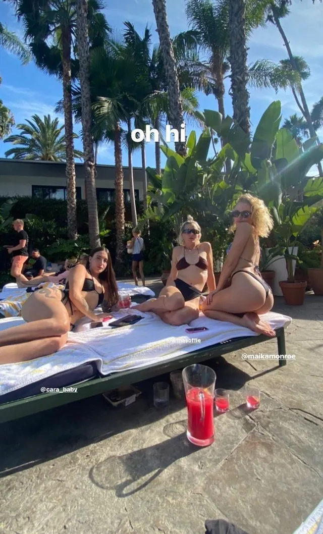 Maika Monroe sitting barefoot by a pool with friends.